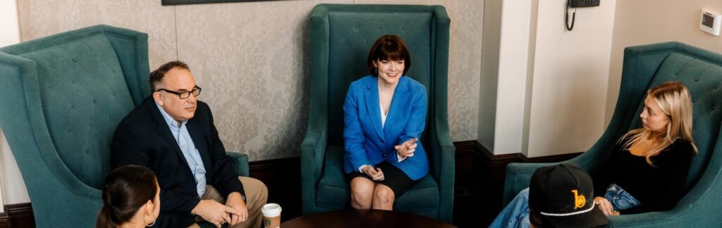 Professors Watkins and Miner, sitting in a circle of large green chairs, talking with students.